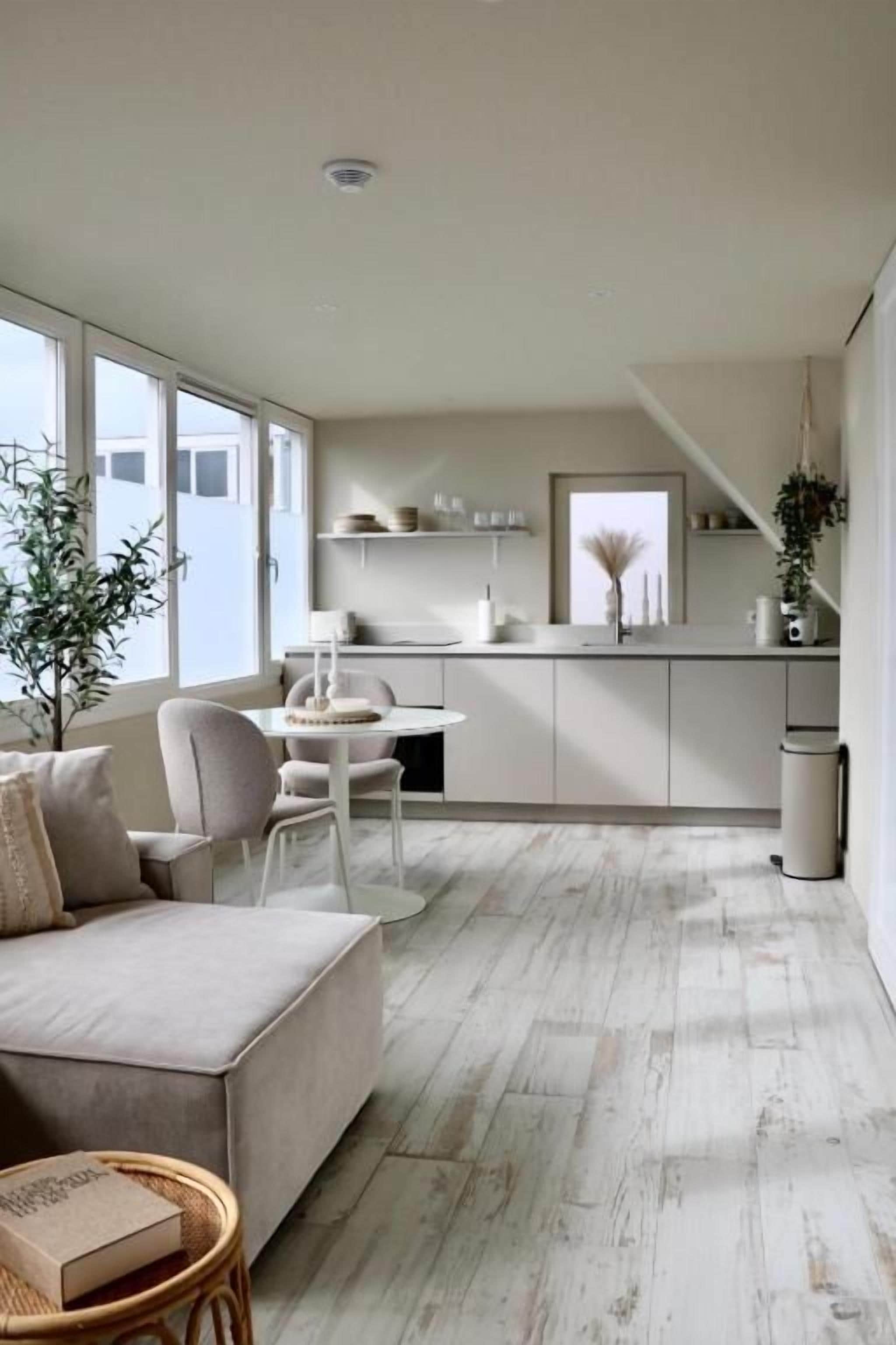 Una sala de estar moderna con un sofá, una mesa de comedor y una zona de cocina con armarios y una ventana.