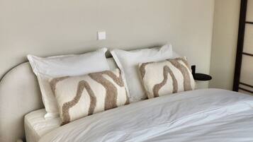A bedroom with a bed, pillows, a nightstand, and a wall-mounted light fixture.