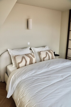 A bedroom with a bed, pillows, a nightstand, and a wall-mounted light fixture. - Breeze Inn B&B (Oegstgeest)