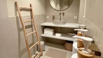 Een badkamer met een houten ladder, een ronde spiegel, een wastafel met wasbak en een handdoekhouder.