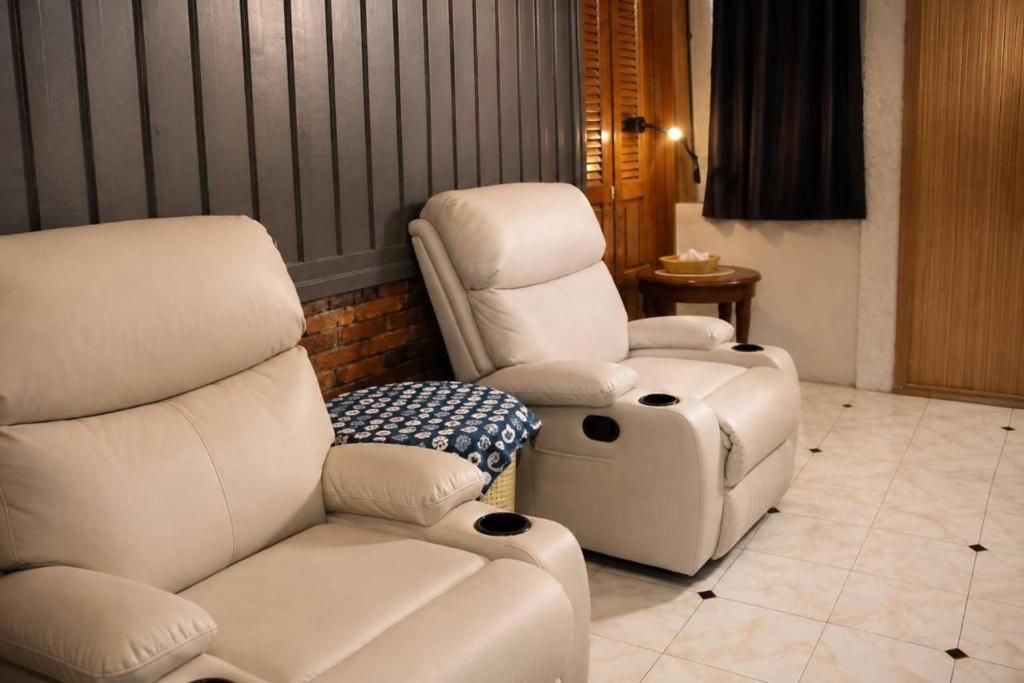 Una habitación con sillón de masaje, una pequeña mesa con lámpara y pared de ladrillo.