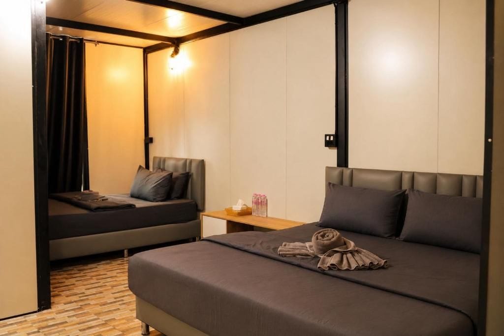 Una habitación de hotel con cama, una zona de descanso más pequeña, una mesita de noche de madera y una lámpara fijada a la pared.