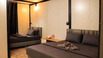 Una habitación de hotel con cama, una zona de descanso más pequeña, una mesita de noche de madera y una lámpara fijada a la pared.