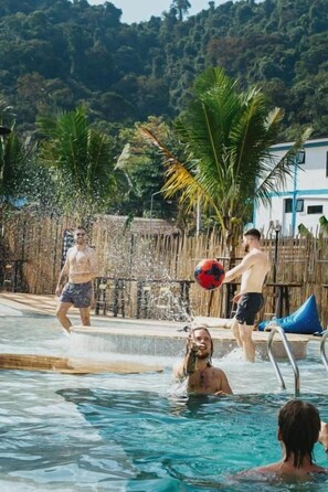 A pool area with people playing, a wooden fence, and a building in the background.