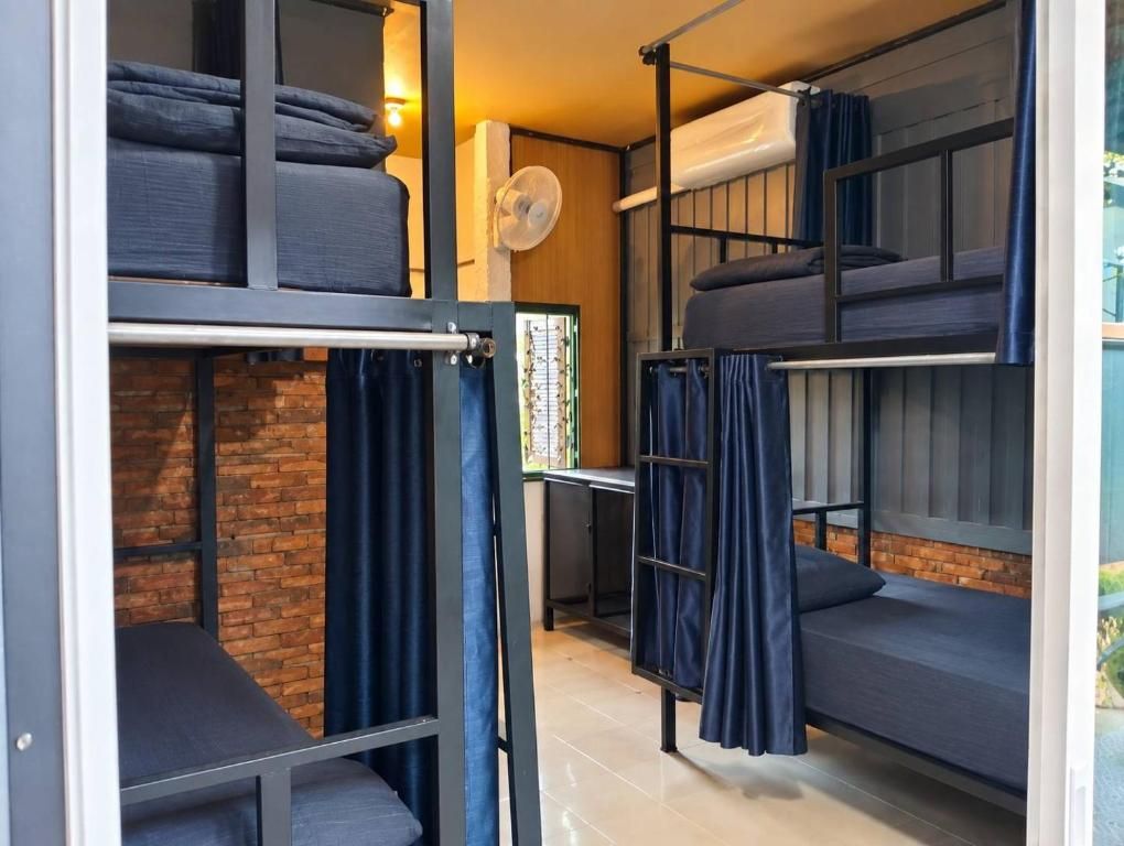 A dormitory-style room with bunk beds, a fan, and a brick wall.