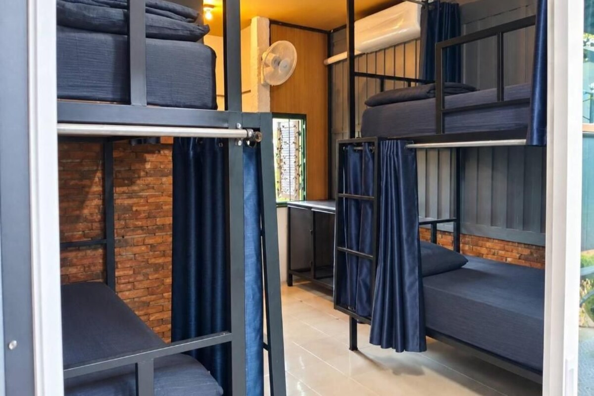 A dormitory-style room with bunk beds, a fan, and a brick wall.