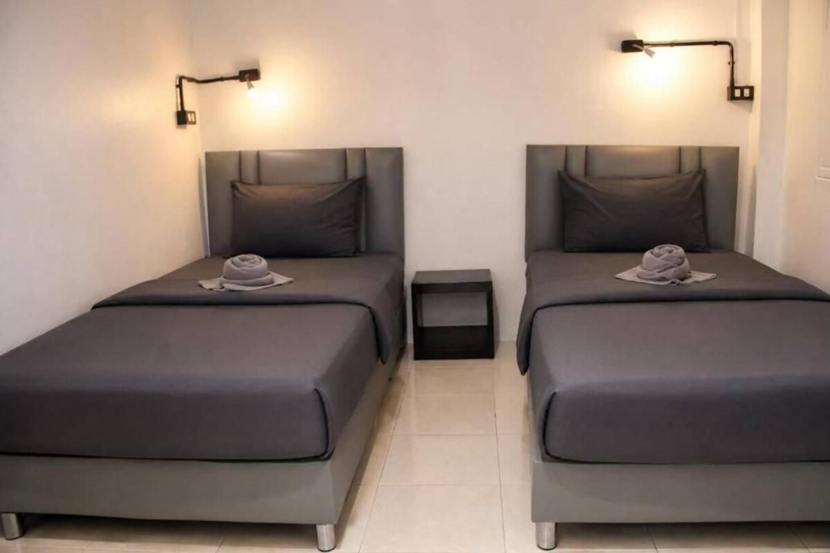 A room with two beds, each with a headboard and a pillow, and a small bedside table between them.