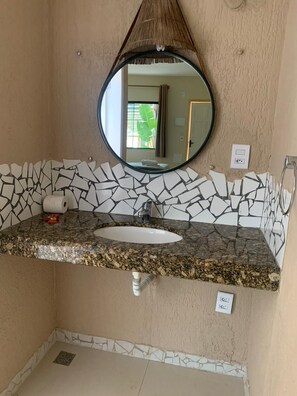 Un bagno con un piano di lavoro in granito, un lavandino bianco, uno specchio rotondo e uno schienale in mosaico.