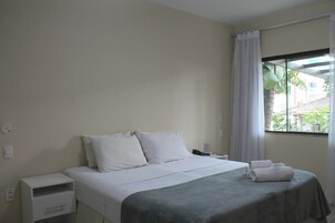 Una cama bien hecha con sábanas blancas, una mesita de noche con un teléfono y una ventana con vistas a zonas verdes.
