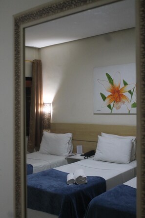 Camera d'albergo con due letti, un comodino con il telefono e un quadro floreale appeso al muro.