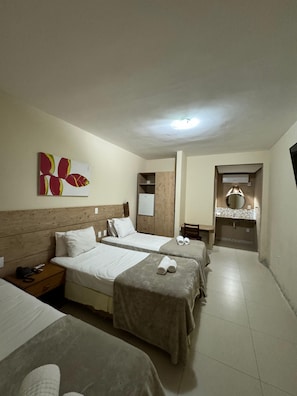 Habitación de hotel con dos camas, cabecero de madera, mesita de noche con teléfono, espejo y baño con lavabo y espejo.