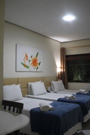 Una camera d'albergo con due letti, un tavolo e un quadro con fiori al muro.