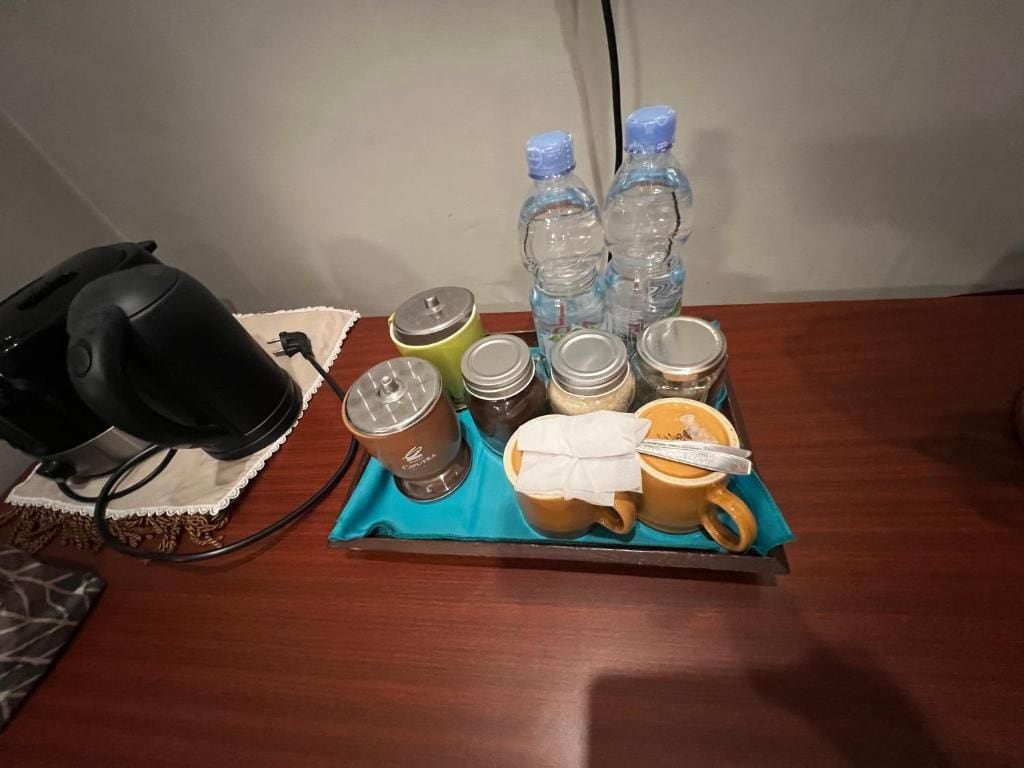 Una bandeja con diversos objetos, entre ellos una cafetera, tazas, botellas y frascos, sobre una mesa de madera.