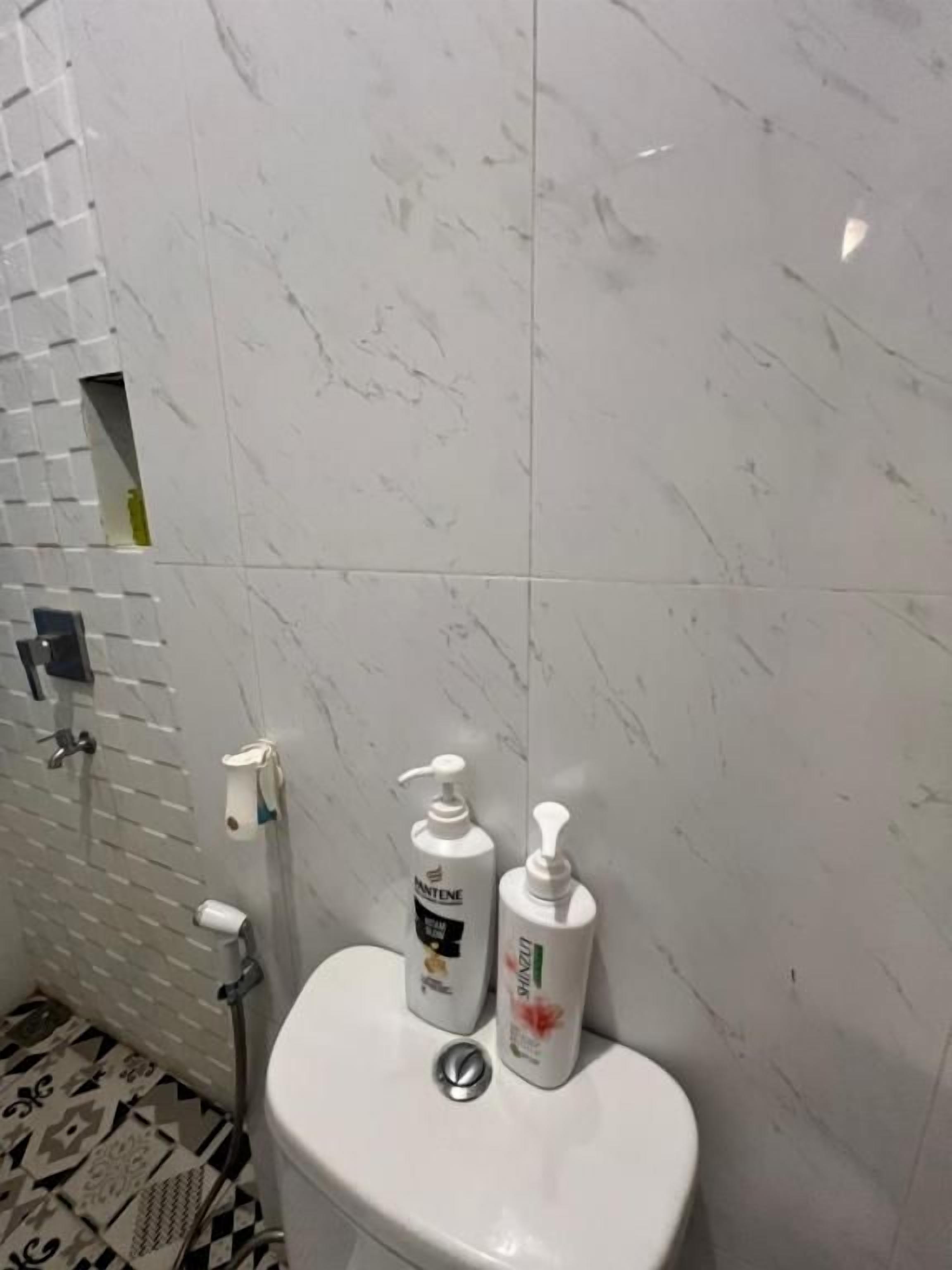 A bathroom with a toilet, a hand soap dispenser, and a bottle of shampoo.