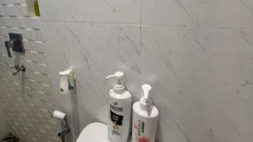 A bathroom with a toilet, a hand soap dispenser, and a bottle of shampoo.