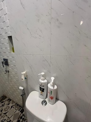 Un baño con inodoro, dispensador de jabón para manos y botella de champú.