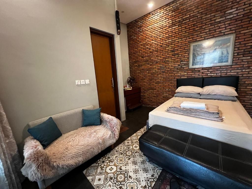 Un dormitorio con pared de ladrillo, cama con almohadas, sofá con manta mullida y alfombra estampada.