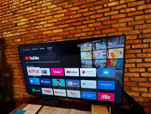 Televisor instalado en una pared de ladrillo mostrando diversas plataformas de transmisión.