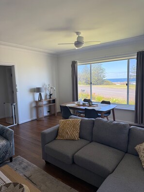 Ein modernes Wohnzimmer mit einem grauen Sofa, einem Esstisch und Blick auf den Ozean.