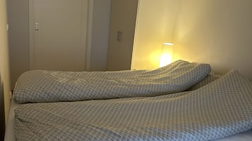 En seng med grå madras og puder, en hvid dør og et garderobeskab.