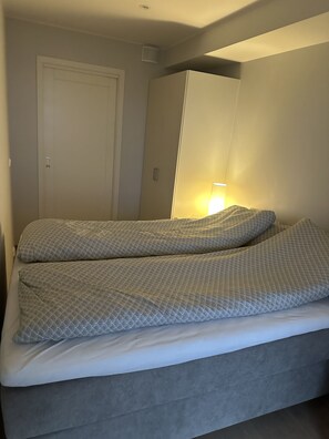 En seng med grå madras og puder, en hvid dør og et garderobeskab.