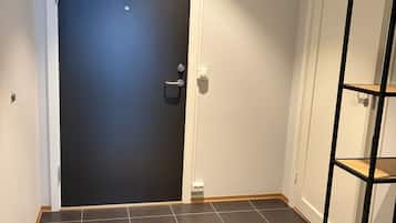 Et værelse med en mørk dør, en hvid væg, et flisegulv og en reol i træ.