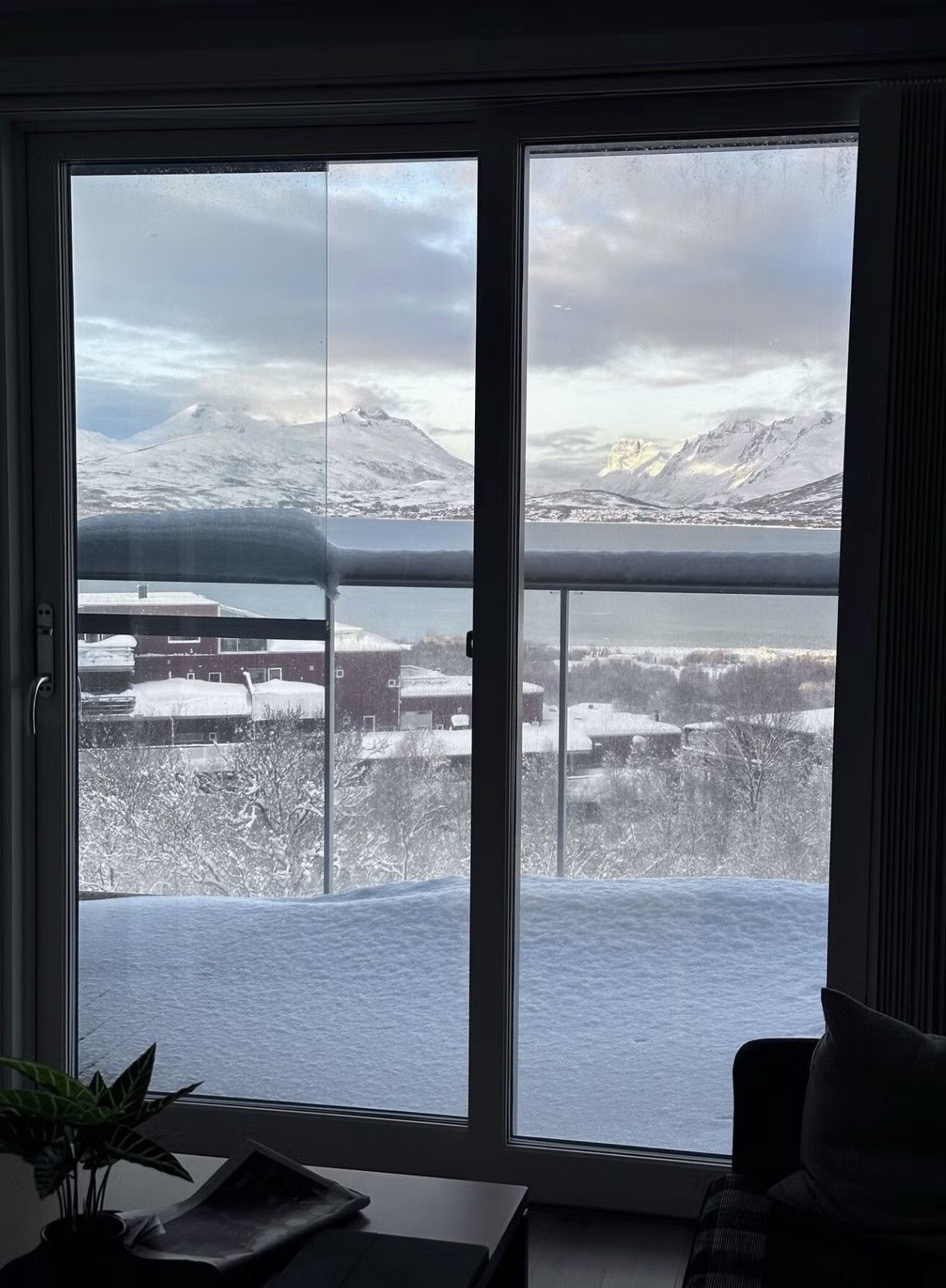 Een kamer met een groot raam, uitzicht op een besneeerd landschap met bergen en een waterpartij.