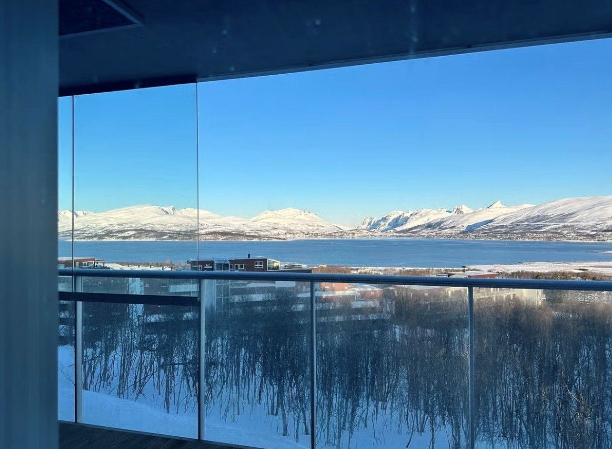 A view from a window overlooking a calm lake with snow-capped mountains in the distance.