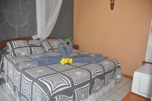 A bed with a patterned bedspread, a decorative towel, and a flower. - Hostal y Cabanas Anakena (Hanga Roa)