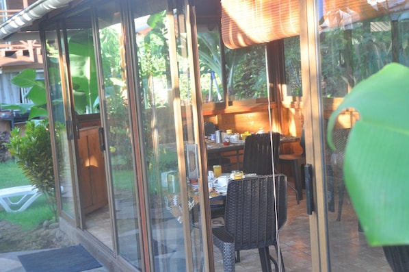A glass-enclosed patio area with a dining table, chairs, and various items on the table. - Hostal y Cabanas Anakena (Hanga Roa)