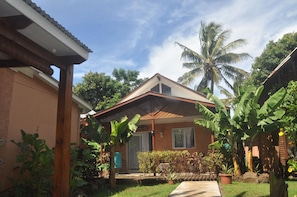 A residential house with a sloped roof, a covered porch, and a well-maintained garden with various plants and a palm tree. - Hostal y Cabanas Anakena (Hanga Roa)