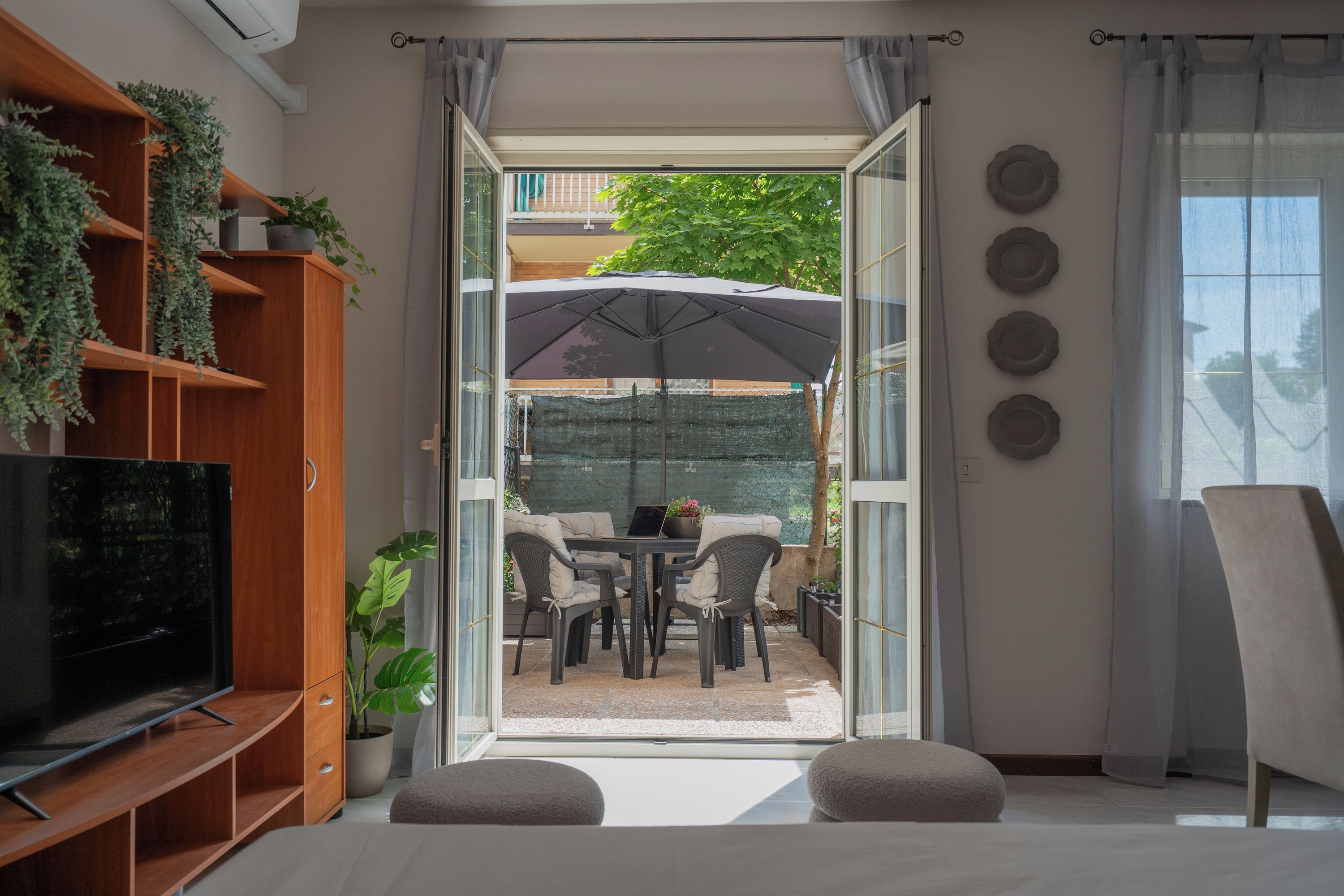 A modern living room with a television, wooden shelving, and a glass door leading to an outdoor patio with a table and chairs.
