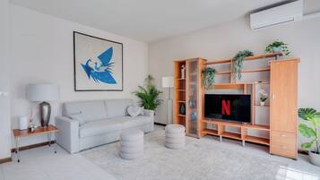 Un soggiorno moderno con un divano grigio, una TV a schermo piatto e un mobile porta TV in legno con piante.