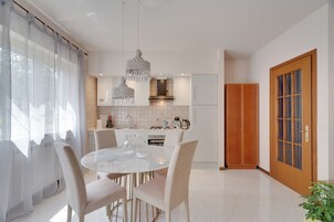 Una cocina moderna con armarios blancos, una mesa de comedor redonda y luces colgantes.