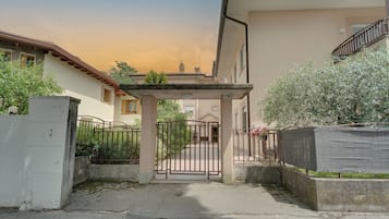 Una entrada cerrada a un área residencial con un cartel de número de edificio, un camino de hormigón y una puerta de metal.