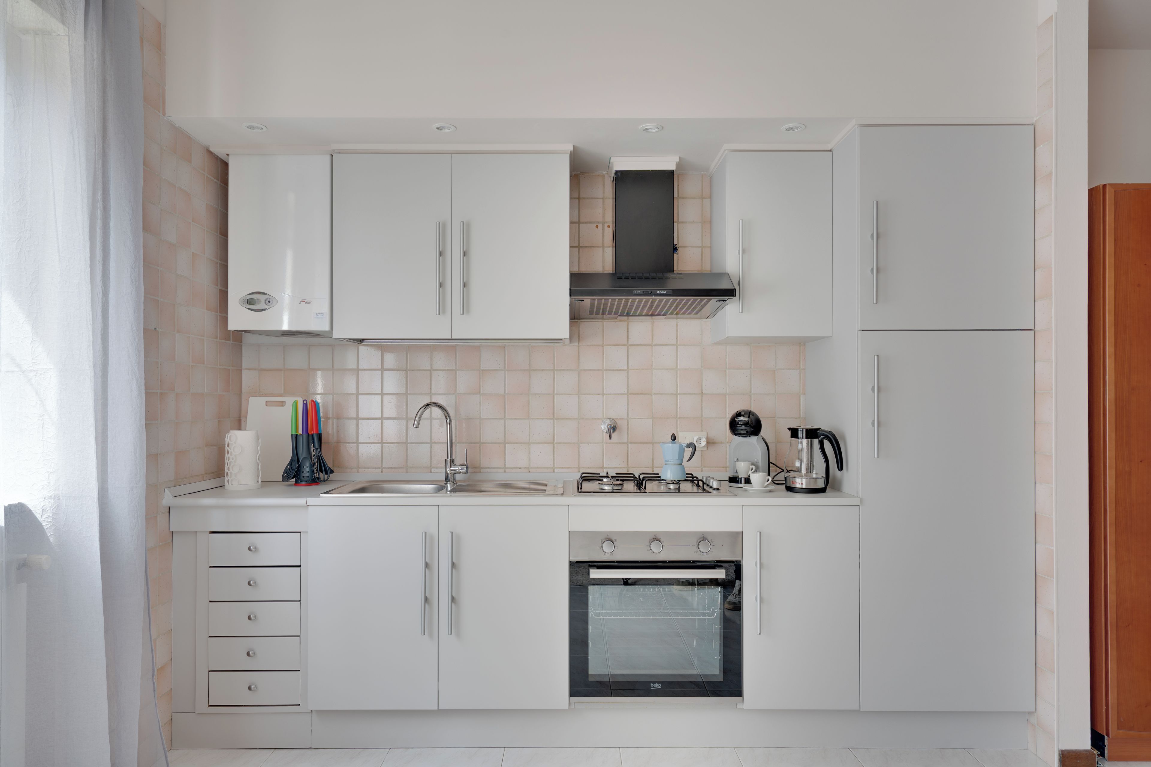 Una cucina moderna con mobili bianchi, un lavello in acciaio inossidabile, un piano cottura a gas e un forno integrato.