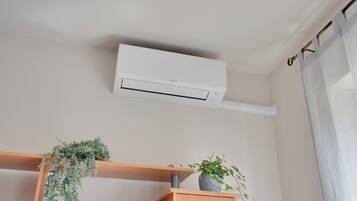 A room with a white air conditioning unit mounted on the wall, wooden shelves with plants, and a curtain on the window.