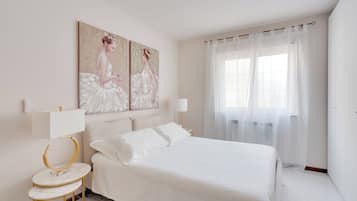 Un dormitorio con una cama, dos mesitas de noche, una lámpara de pared, un cuadro y un ventanal con cortinas translúcidas.
