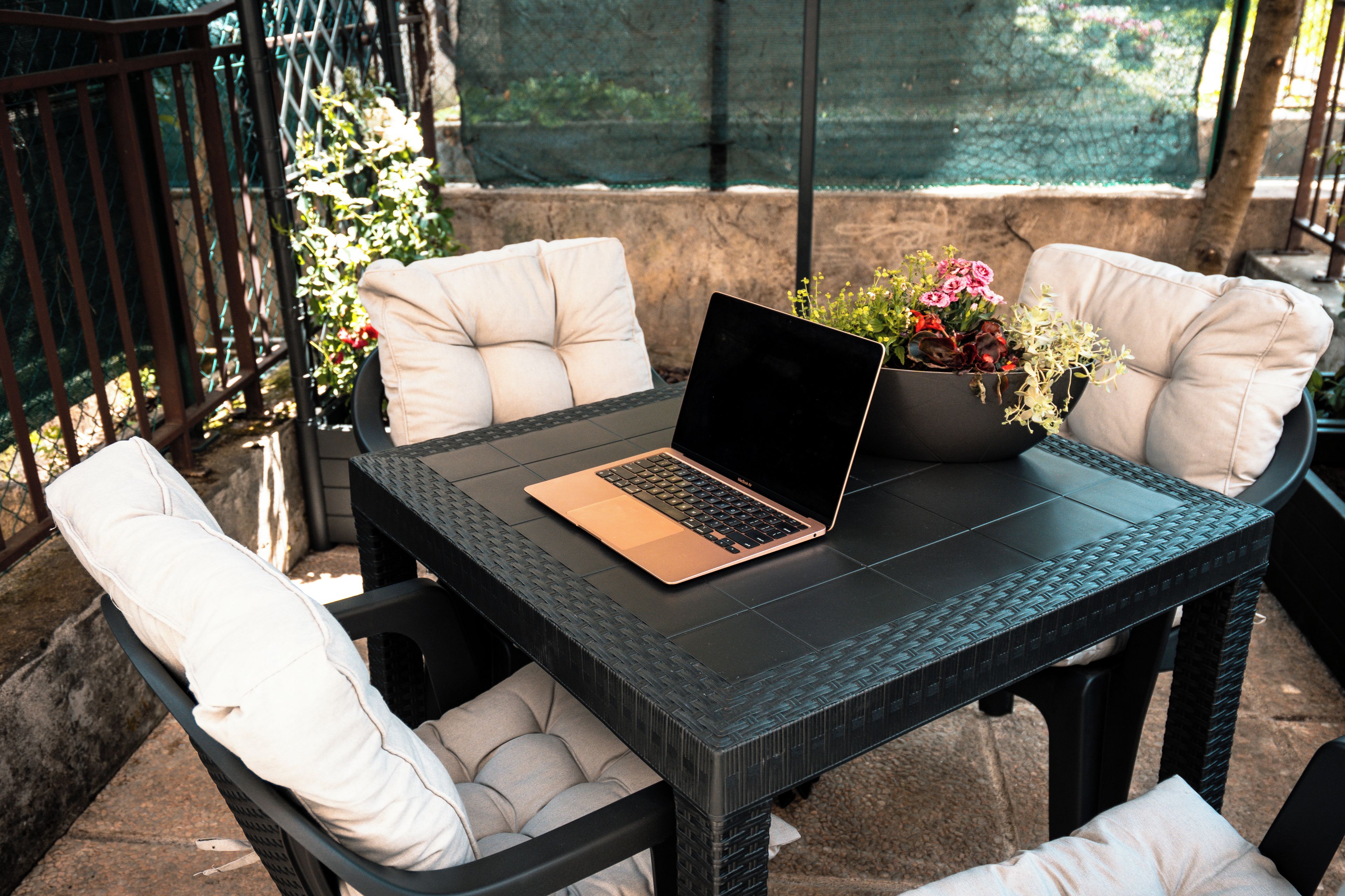 Una mesa con una computadora portátil, rodeada de sillas con cojines, y una planta en maceta sobre la mesa.