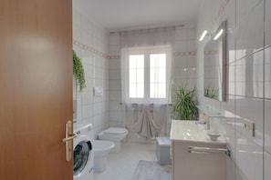 Un baño moderno con lavadora, dos inodoros, un lavabo y un espejo grande.