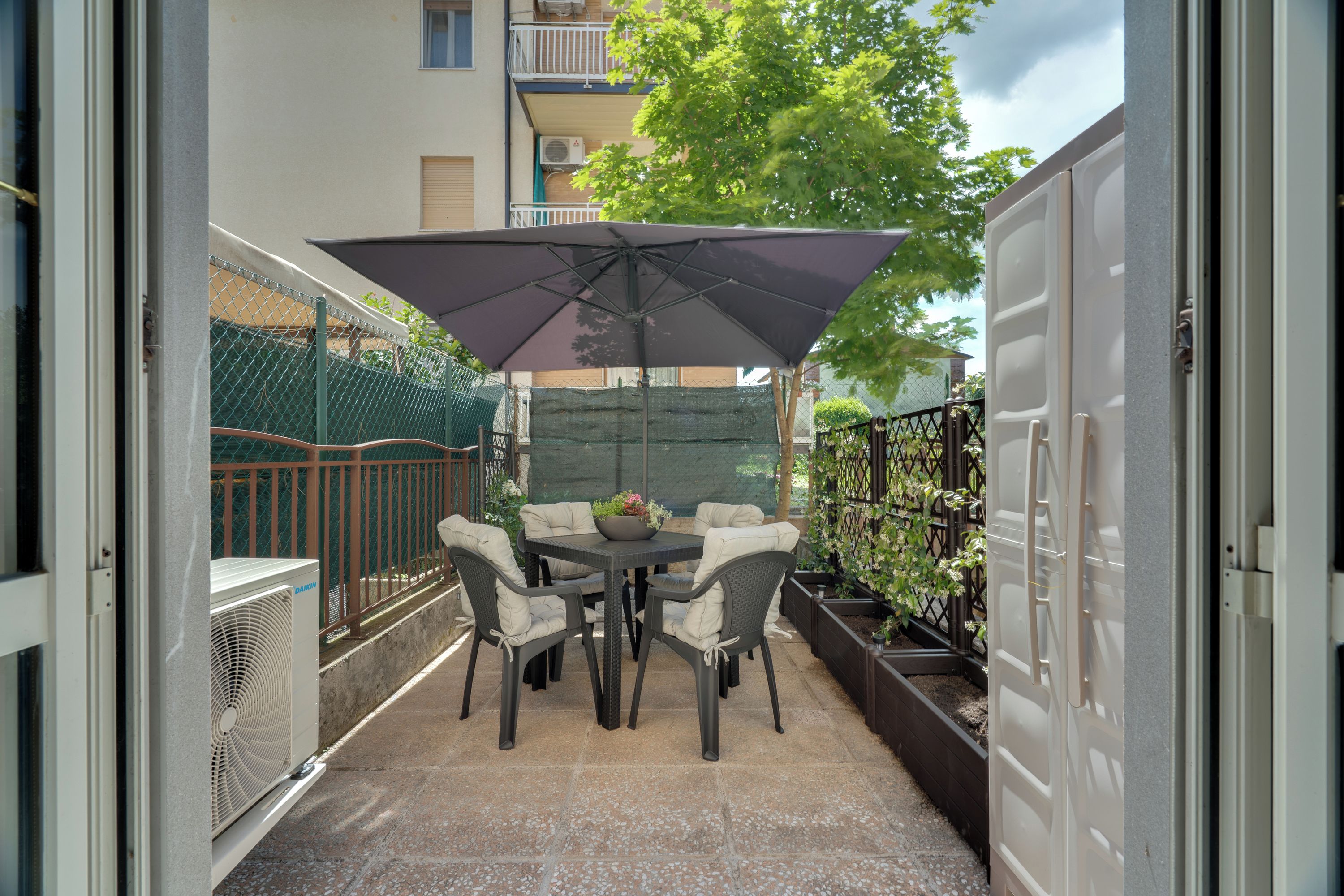 Un patio con una mesa, sillas, un paraguas grande y una planta en maceta.