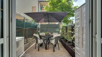 Un patio con una mesa, sillas, un paraguas grande y una planta en maceta.
