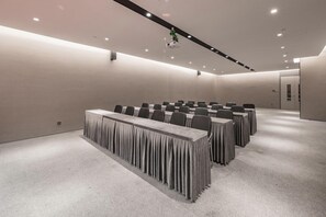 Ein Konferenzraum mit Tischen und Stühlen, einem Teppichboden und eingelassener Deckenbeleuchtung.