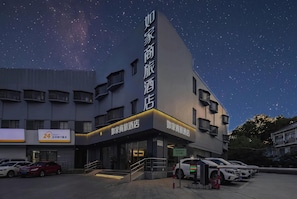 A hotel with a modern design, featuring a prominent vertical sign with Chinese characters, a well-lit entrance, and a parking area with several cars. - Homeinn Selected (Shanghai)