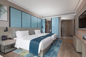 Habitación de hotel moderna con una cama grande, mesitas de noche, un escritorio, un televisor y un baño visible a través de una puerta abierta.