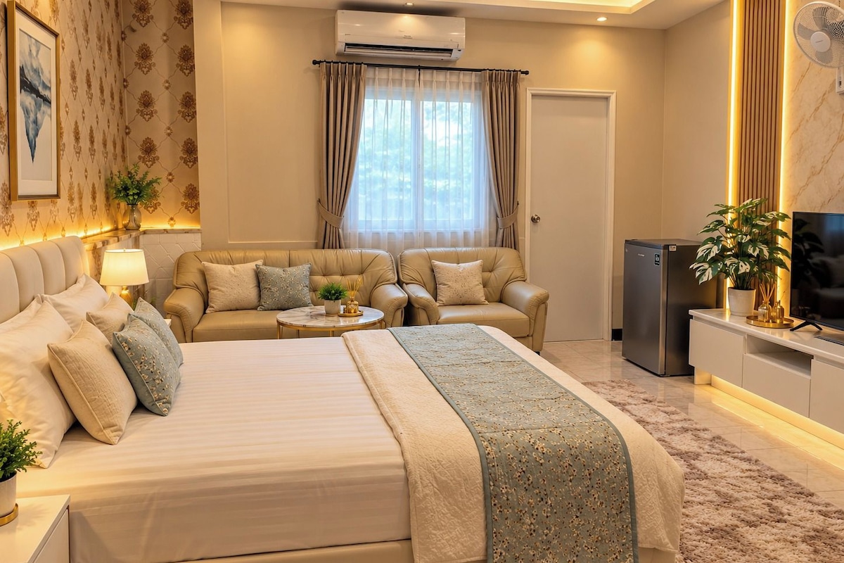 Habitación de hotel con cama, dos sofás, televisor, refrigerador y una planta en maceta.
