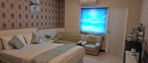 A bedroom with a bed, a sofa, a small table with a plant, and a window with a view. - Jomtien Beach Stay (Pattaya)