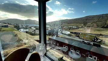 A room with a large window offering a view of a coastal town, a chair, and a potted plant.