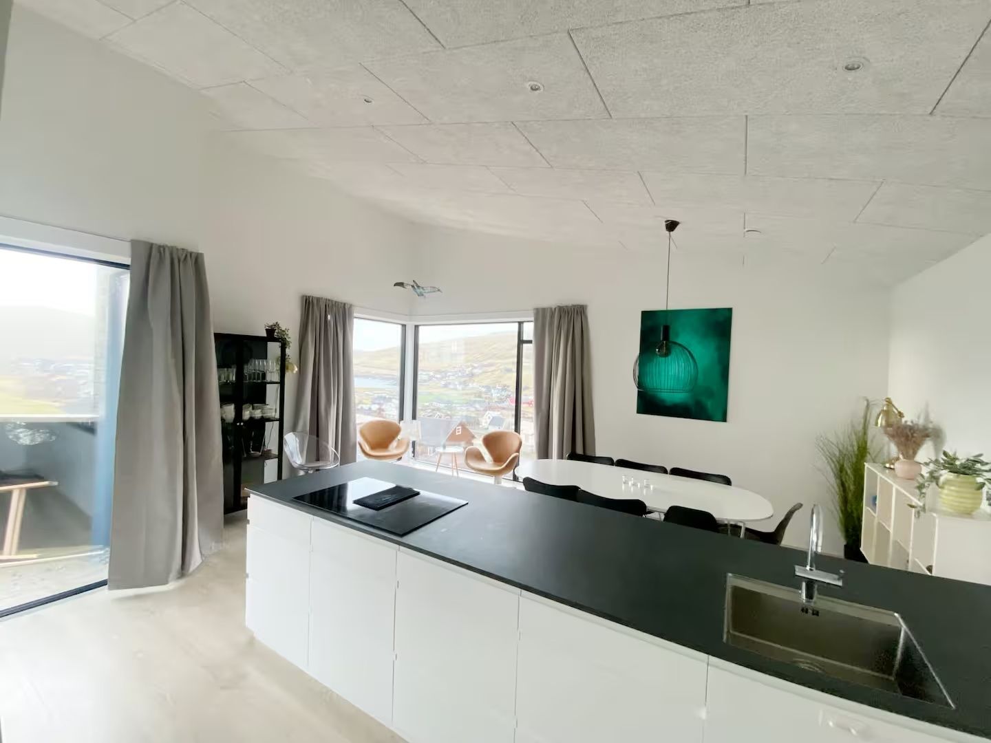 Una cocina moderna con una isla central, zona de comedor con sillas y grandes ventanales con vistas.