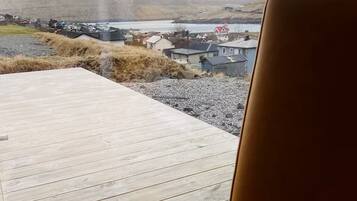 A view from a window with a wooden deck and a chair, overlooking a rural landscape with houses and hills.